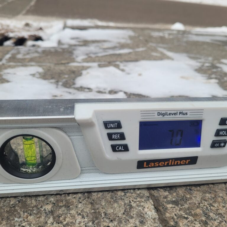 Zbliżenie - poziomica elektroniczna leży na lekko zaśnieżonym chodniku.