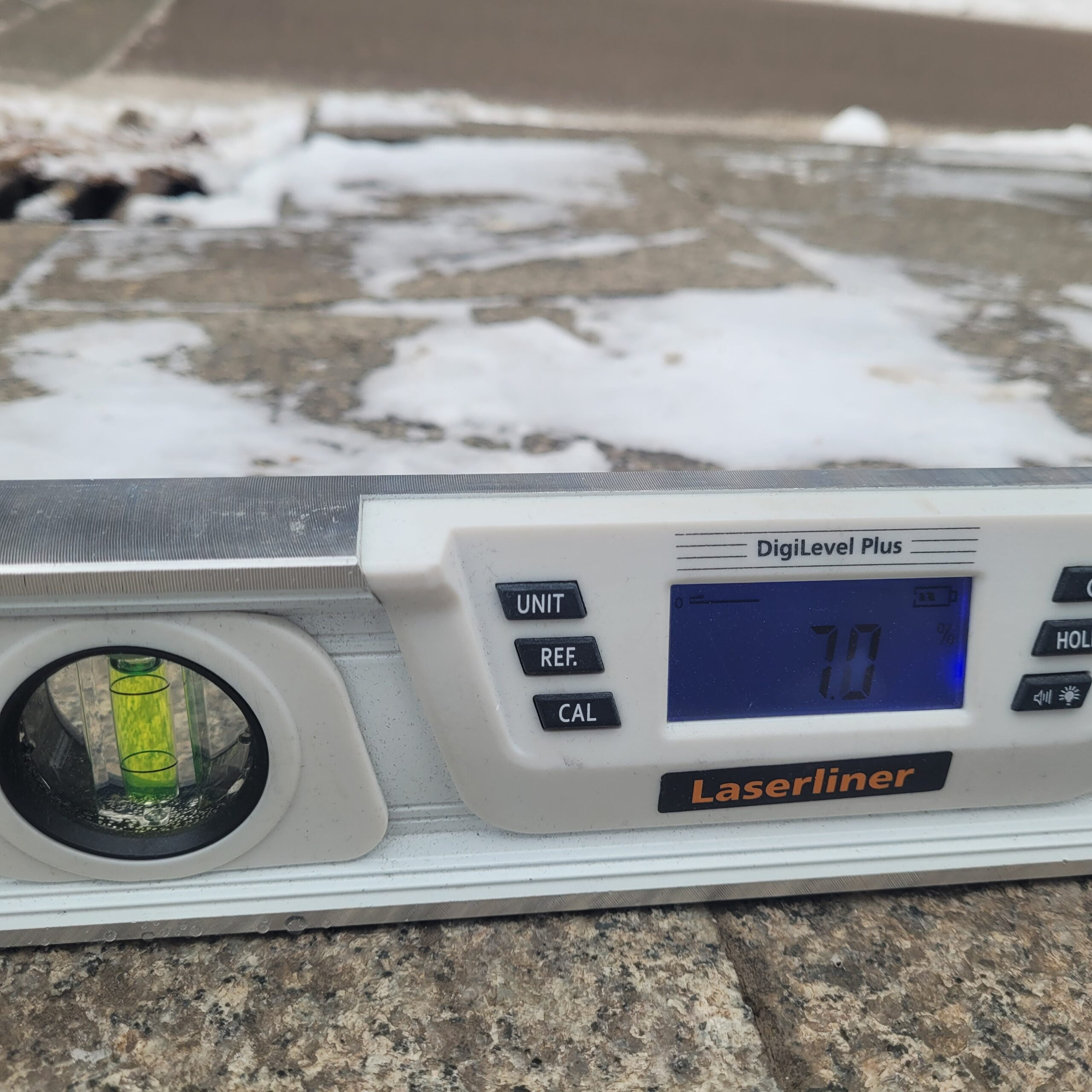 Zbliżenie - poziomica elektroniczna leży na lekko zaśnieżonym chodniku.