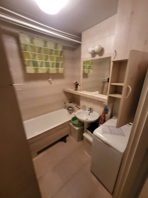 Widok na starą łazienkę. W prawym rogu pralka, obok niej malutka umywalka, pod lewą ścianą wanna.